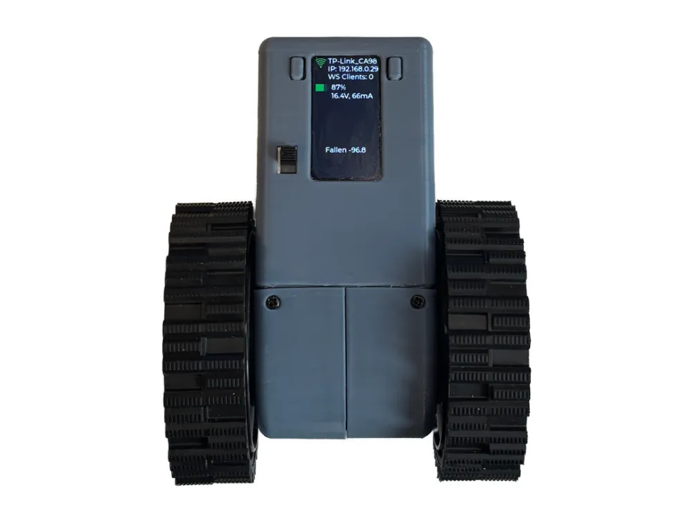 Earlier balancing robot revision, front view: grey printed enclosure with OLED showing WiFi, IP, battery, and fallen tilt status; wide treaded wheels and power switch.