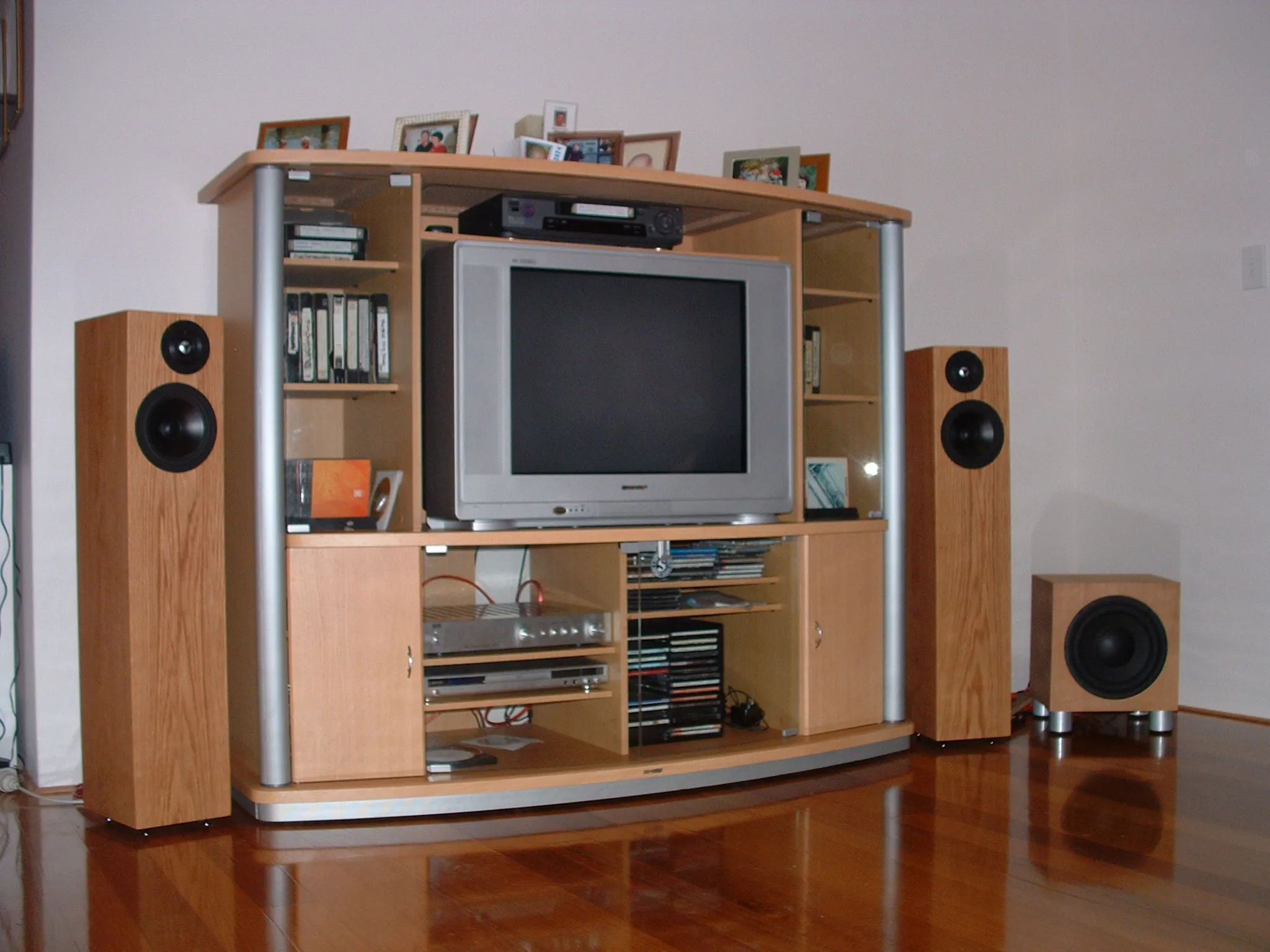 Finished light-wood DIY floorstanding speakers and matching subwoofer flanking a large wooden entertainment center with CRT TV and stereo gear in a living room.