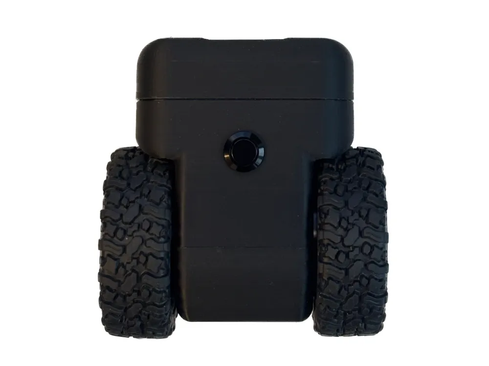 Front view of the self-balancing robot: symmetrical black 3D-printed body with central circular sensor or button, two wide knobby RollerCAN tires, and horizontal seam at the top cap.